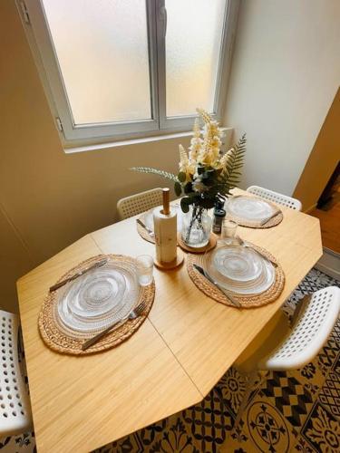 une table en bois avec deux assiettes et un vase de fleurs dans l'établissement Le Rêve Azuréen, à Fontainebleau