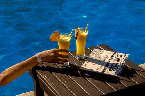 a person holding two drinks on a table next to a pool at El Clan Hostel in Puerto Viejo