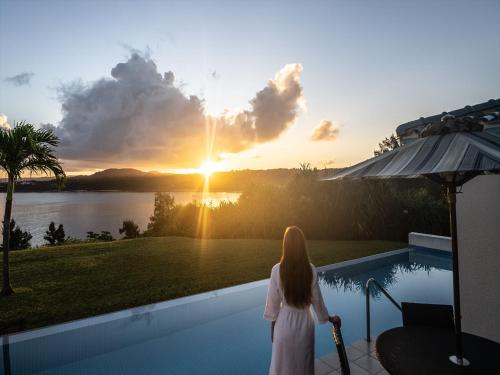 a woman standing by a swimming pool looking at the sunset at Oriental Hills Okinawa in Onna