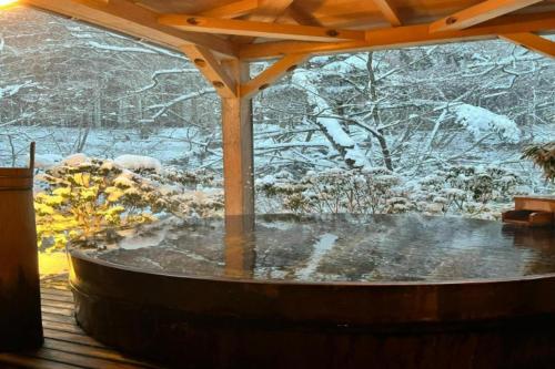 a hot tub on a deck with snow covered trees at Shionoyu Onsen Rengetsu in Nasushiobara