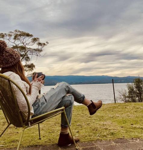 a woman sitting in a chair next to a lake at The Gums - Bruny Island in Woodbridge
