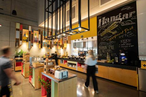 a woman walking inside of a restaurant with a counter at Atura Adelaide Airport in Adelaide
