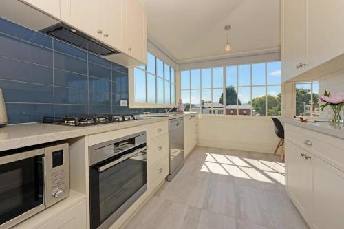 a large kitchen with white cabinets and blue tiles at The Lollyshop Apartment in Battery Point in Hobart