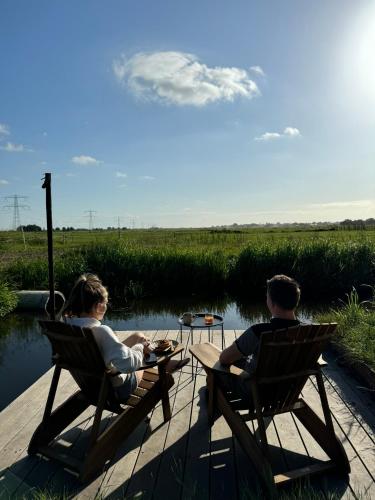 a man and a woman sitting in chairs on a dock at TinyHouse Noorderlicht in Haastrecht