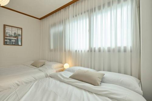 two white beds in a room with a window at Haru Stay in Seoul