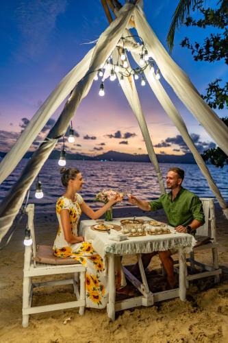 a man and a woman sitting at a table on the beach at Soul Villas - Beachfront Private Pool Villas, Phuket Nature Retreat in Panwa Beach