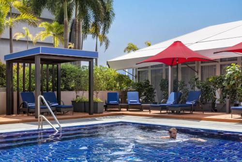 a person swimming in a swimming pool with chairs and umbrellas at Dusit Thani Manila in Manila
