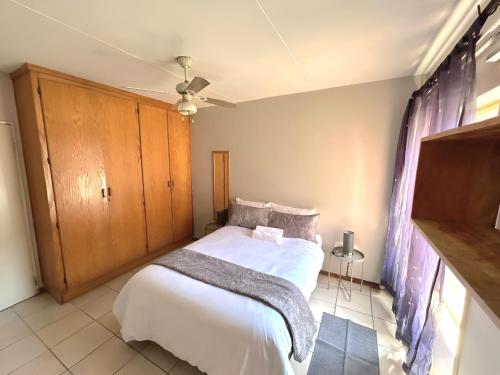 a bedroom with a white bed and a wooden cabinet at Cozy secure apartment in Bloemfontein