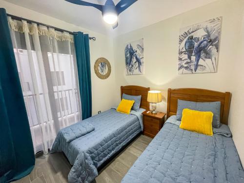two beds in a bedroom with blue and yellow pillows at Casa Paraiso in Caleta De Fuste