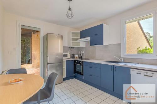 une cuisine avec des placards bleus, une table et une fenêtre dans l'établissement Maison Évasion - Confort, Bureau, Jardin & Barbecue, à Oullins