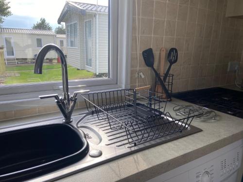 a kitchen sink with a dish drying rack next to a window at Coastal Caravan Holidays - Nightingale 8 in Tunstall