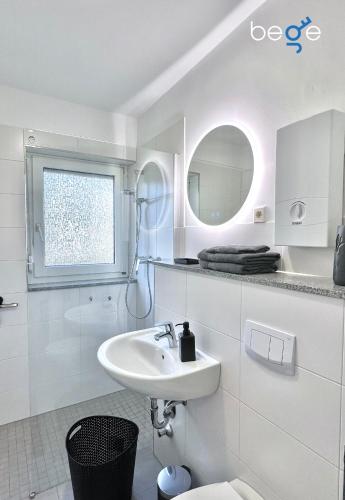 a white bathroom with a sink and a mirror at BEGE APARTMENTS Company Base in Störringen