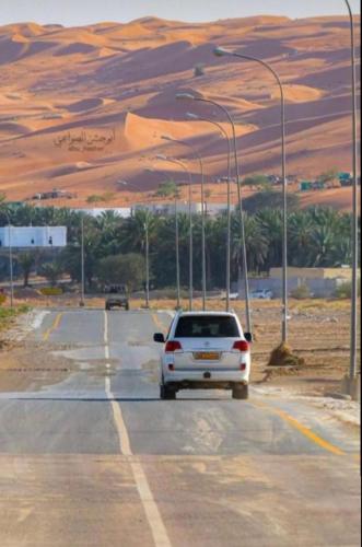 a white car driving down a road with street lights at Bidiya oasis in Al Raka