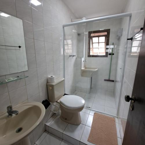 a white bathroom with a toilet and a sink at Recanto Do Sol Bertioga in Bertioga