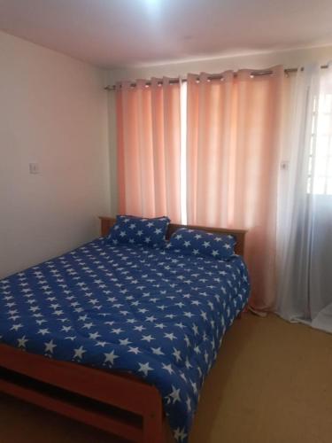a bedroom with a bed with a blue comforter and a window at Elgon Apartment in Kahawa