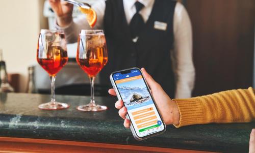 a person holding a cell phone at a bar with wine glasses at Forte Family Village - Azzurro Club in Sella Nevea