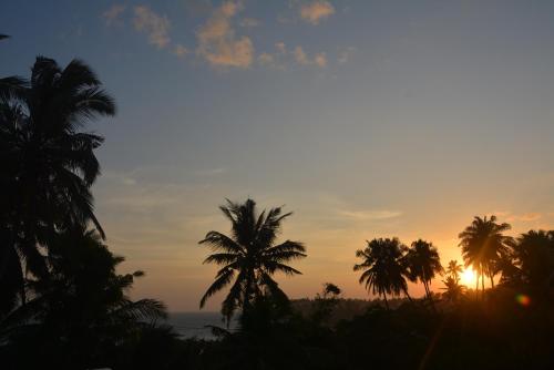a sunset with palm trees in front of the ocean at Sea View Tourist Inn in Tangalle