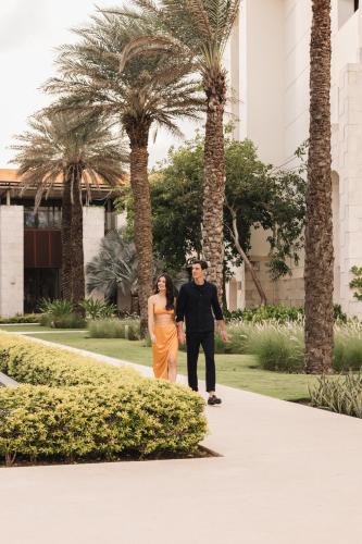 a man and a woman walking down a sidewalk with palm trees at Unico Hotel Riviera Maya Adults Only in Akumal