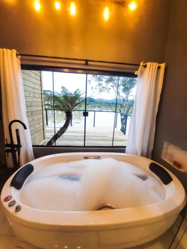 a bath tub in a room with a large window at Cabana do Lago com passeios a cavalo gratuito in Urubici