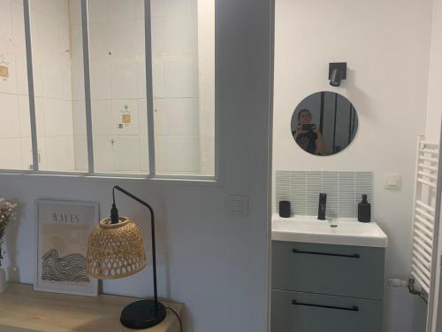 La salle de bains est pourvue d'un lavabo, d'un miroir et d'une lampe. dans l'établissement Charmant T2 meublé plein centre et proche plage, à Dinard