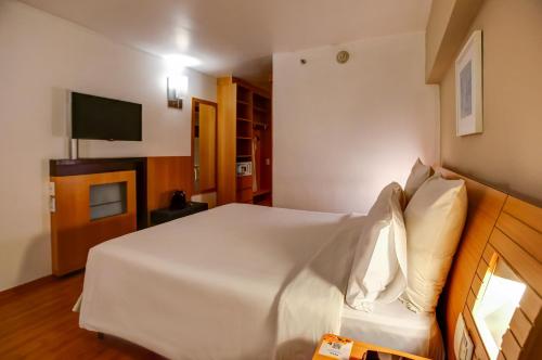 a bedroom with a white bed and a television at Novotel RJ Santos Dumont in Rio de Janeiro