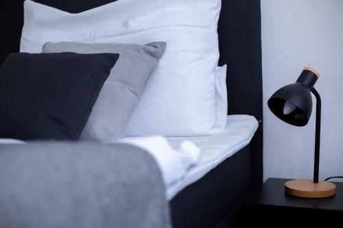a bed with white pillows and a black lamp on a table at BEST STAY CityAppartment Hünfeld- SmartTV FreeWlan Balkon, in wenigen Minuten am Bahnhof, Innenstadt und doch ruhig gelegen - ideal für Paare oder Geschäftsreisen in Hünfeld