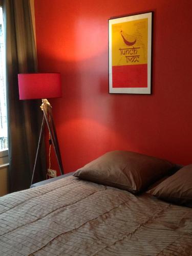a bedroom with a red wall with a bed and a lamp at Côté Saint-Léonard - Honfleur in Honfleur