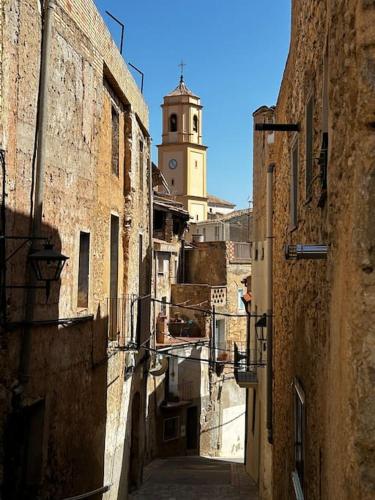 an alley with a clock tower in the background at Rural Stone House with wood fireplace in Pinell de Bray