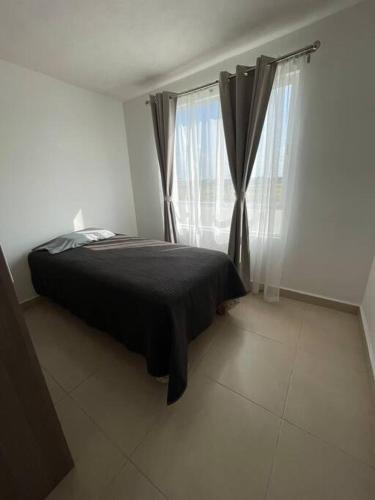 a bedroom with a bed with a black blanket and windows at Alojamiento en León in Santa Gertrudis
