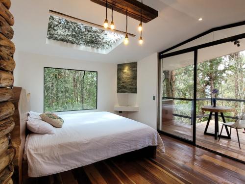 Un dormitorio con una cama y grandes ventanales. en Cabaña Aventurina- La pascana Ecolodge Entorno natural excepcional, conexión con la naturaleza y avistamiento de aves, Ubicado a 3km del metrocable y Parque Arvi, Guarne, en Mazo