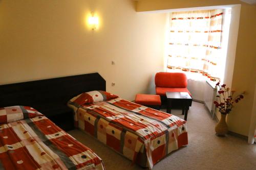 a bedroom with two beds and a chair and a window at Хотел Кипарис, Враца in Vratsa