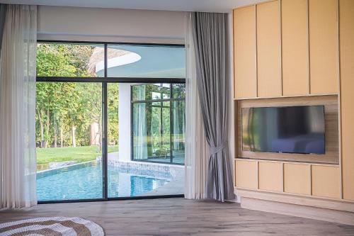 a living room with a tv and a large window at Villa De Leaf River Kaeng Krachan in Phetchaburi