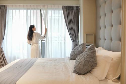 a woman standing in a bedroom looking out the window at THEA Private Suites by TH District in Bangkok
