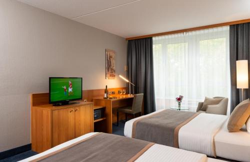 a hotel room with two beds and a television at Leonardo Hotel Köln Bonn Airport in Cologne