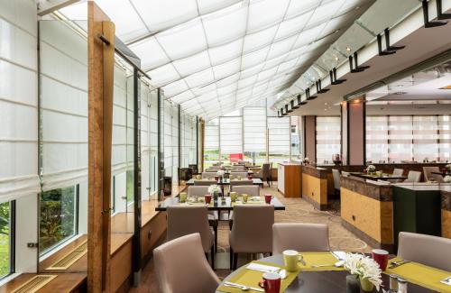 a restaurant with tables and chairs and large windows at Leonardo Hotel Köln Bonn Airport in Cologne