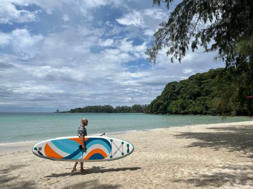 a man standing on a beach holding a surfboard at Koh Kood Club in Ko Kood