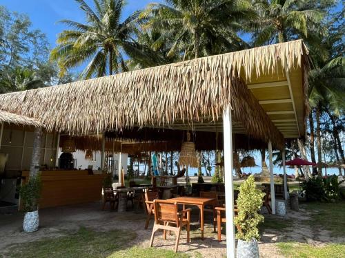 a restaurant with tables and chairs under a thatched roof at Koh Kood Club in Ko Kood