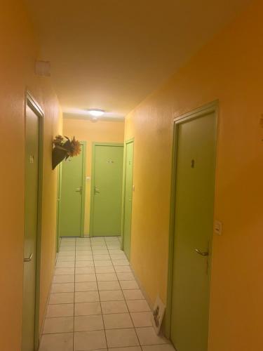 an empty hallway with green doors and a tile floor at Le Manteau Bleu in Béziers