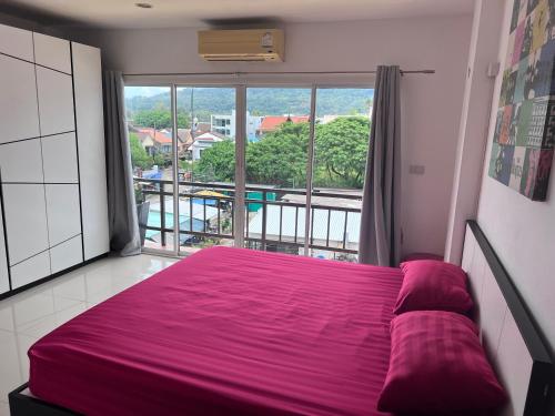 a bedroom with a purple bed and a large window at KC Kamala Guesthouse in Kamala Beach