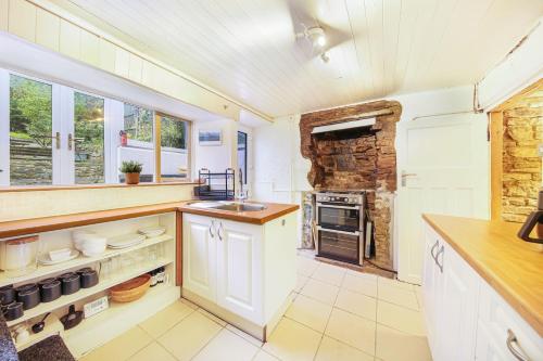 a kitchen with white cabinets and a stone wall at Host & Stay - Batemill Cottage in Birch Vale