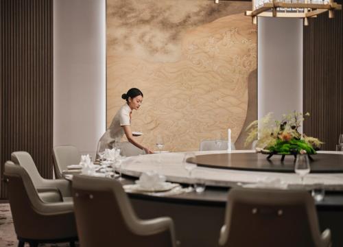 a woman standing behind a table in a restaurant at The Azure Ningbo, Vignette Collection in Ningbo