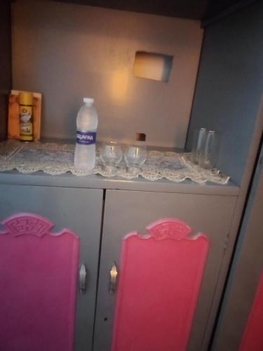 a counter with glasses and a bottle of water and two pink chairs at Nubian Life Nile View in Aswan