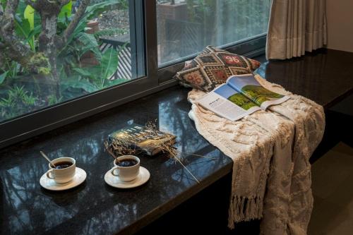 a table with a book and two cups of coffee at SaffronStays Red Brick House, Panchgani - rustic villa with huge lawn and terrace in Panchgani
