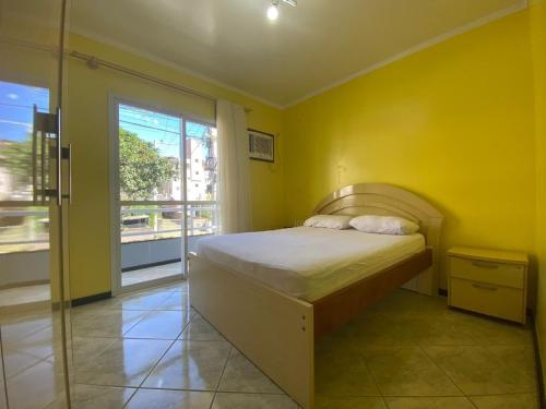 a yellow bedroom with a bed and a window at B149 - Ampla casa no centro de Bombinhas - SC in Bombinhas