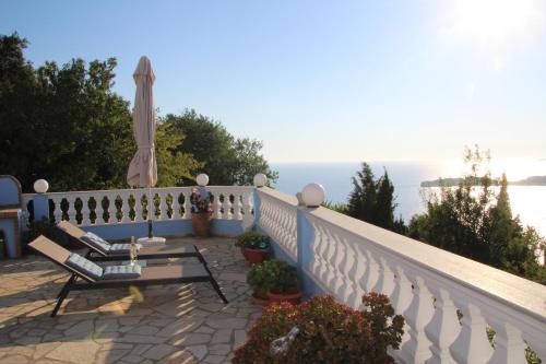 a balcony with chairs and an umbrella and the ocean at Villa Bettina 1st floor in Afionas