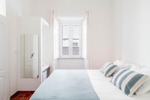 a white bedroom with a bed with blue and white pillows at Guesthouse Casa Felicia in Montes de Alvor