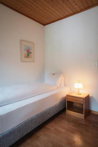 a white bedroom with a bed and a table with a lamp at Hotel Haus Schönstatt contactless-Check-In in Brig