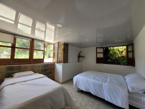 une chambre avec deux lits et deux fenêtres dans l'établissement La Pascana Ecolodge APTO BARRANQUERO frente al parque Arví Entorno natural excepcional, reserva natural, áreas protegidas, conexión con la naturaleza y avistamiento de aves a 3km del metrocable Guarne, à Guarne