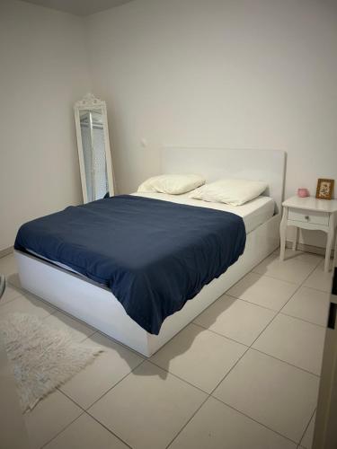 - une chambre blanche avec un lit et une couverture bleue dans l'établissement Appartement T2 récent Sabine, à Montpellier
