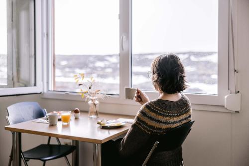a woman sitting at a table looking out a window at Aska, Modern Cabin in Myvatn